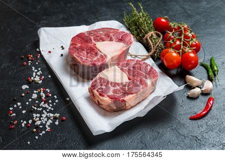 Raw veal shank slices meat and ingredients for Osso Buco cooking on black background, top view