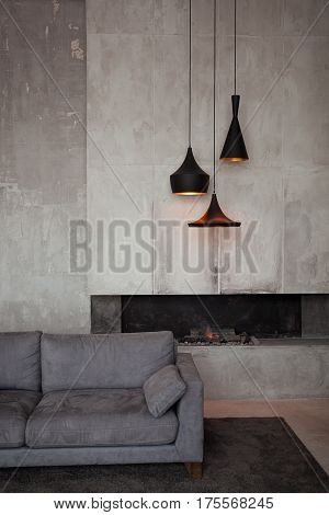 Gray velour sofa in a dark room the bright light from eternal light, and artificial fireplace. Interior loft with concrete walls.