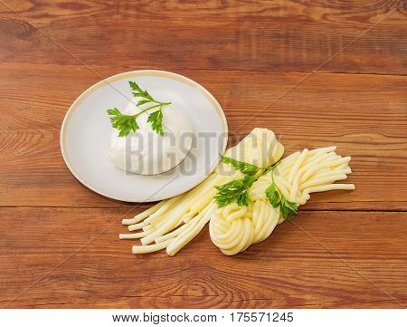 Ball of the fresh mozzarella cheese on the saucer two portion of the mozzarella cheese in the shape of strings twisted to form a plait and twigs of parsley on an old wooden surface
