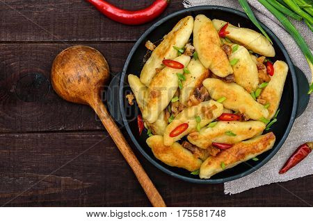 Popular traditional Czech Hungarian German dish: potato knedli (dumplings) with slices of fried bacon spicy red pepper and green onions. Serving on a cast iron pan. The top view