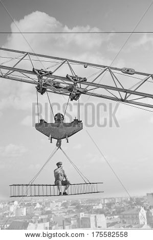 Alone and calm. Black and white shot of a relaxed vintage handyman drinking milk sitting on a crossbar hanging from a construction crane high above the city relaxation peaceful calamity worker concept