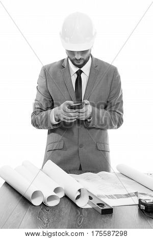 Monochrome Black and white vertical studio shot of a male engineer wearing a hardhat typing on his smart phone. Engineering business people technology connectivity messaging concept.