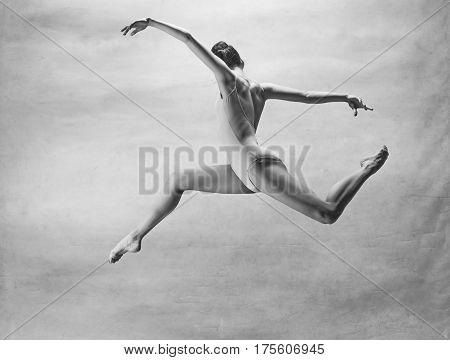 Young beautiful modern style dancer jumping on a studio background. Colorless image