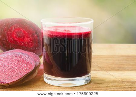Fresh beet juice in glass and sliced beetroot on wooden table blur defocused nature background