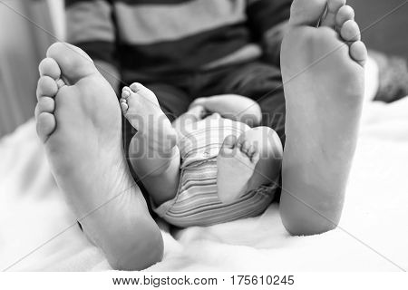 Closeup of huge feet of father and little newborn baby. Big feet of adult and tiny legs of child. Happy parenthood, carefree childhood, family, love, tenderness. In black-and-white, monochrome