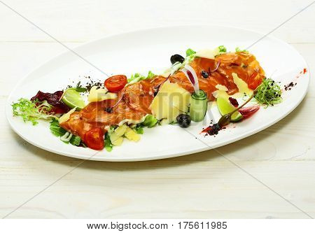 Delicious red fish or salmon fillet slices sashimi garnished with cheese and colorful vegetables on plate on white background. Modern molecular gastronomy
