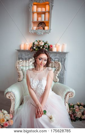 Pretty young bride in pink wedding dress sitting on a luxurious chair. Holding a rose