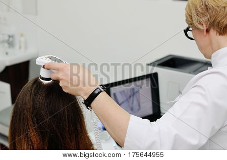 Doctor examines the hairy part of the patient's head - pretty young girl. Trihoskopiya, psoriasis, dandruff, split ends, peeling, dermatology.