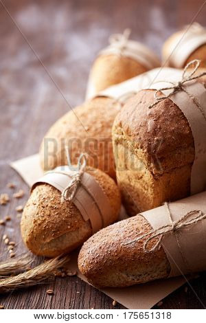 Many different bread in the baking paper and decorative rope on the wooden table, selective focus. Brown background. Table with flour and whole. Natural products and materials. Baker and tasty.