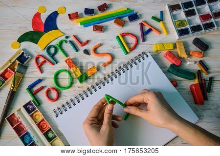 hands make April Fools' Day text made with plasticine on white wooden background