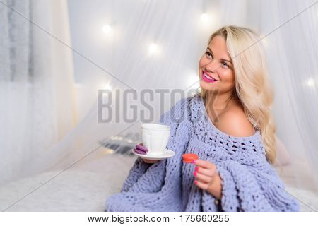 Perfect blonde is sitting with a cup of tea and macaroons