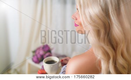 Perfect blonde is sitting with a cup of tea and macaroons