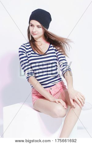 Youth fashion Concepts and Ideas. Stylish Smiling Caucasian Slim Brunette in Hat Posing On White Box in Studion Against White. Vertical Shot