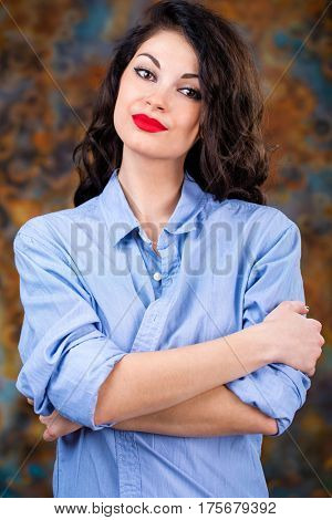 Closeup portrait of young brunette woman in blue shirt, dark studio wall background