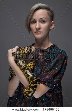 Young woman holding anaconda on gray background