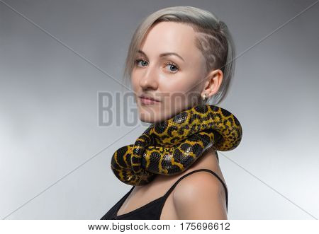 Woman with yellow snake on her neck on gray background