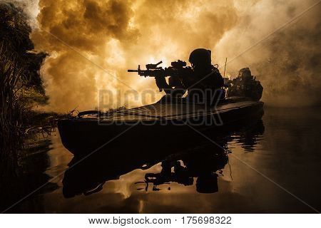 Backlit silhouette of special forces marine operators in military kayak on fire explosion background. Battle operation, bombs exploding