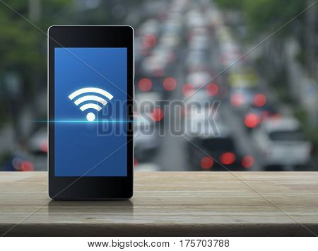 Wi-fi connection icon on modern smart phone screen on wooden table over blur of rush hour with cars and road Technology and internet concept