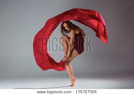 Young beautiful woman dancer in red swimsuit posing on a light grey studio background. Contemporary