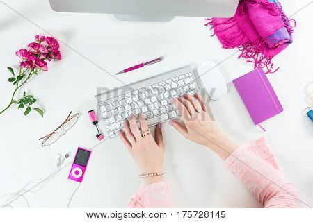 Person working on Computer at White Desk with red and pink Business and Lifestyle Items Top View