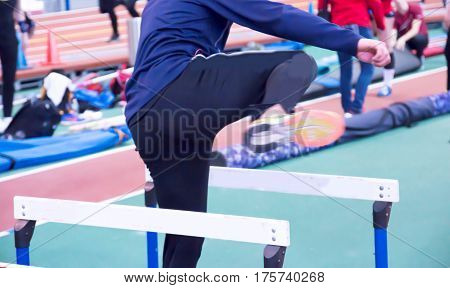 An athlete warms up for their race doing hurdle drills on the infield of an indoor track and field arena