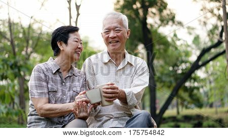 Old Asian Senior Couple Morning Date With Cup Of Coffee In Green Background Park