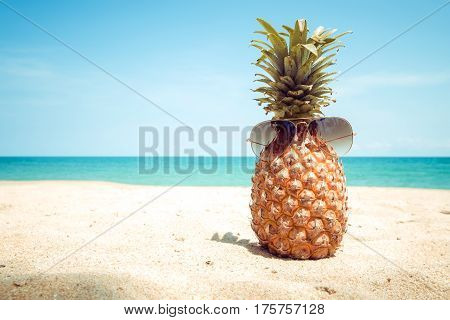 Hipster pineapple with sunglasses on a sandy at tropical beach. concept of fashion in summer. vintage colortone filter effect