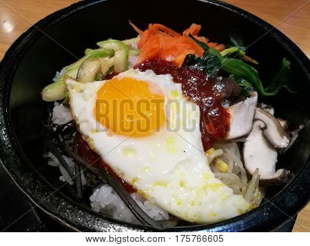 Classic Korea food vegetable Bibimbap hot stone pot rice carrot spinach mushroom cucumber seaweed fried egg and hot spicy chili sauce focus-on-foreground and blur background Asian meal