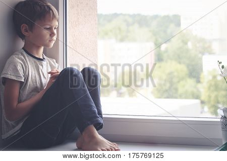 Sad kid sitting on window shield and looking out the window