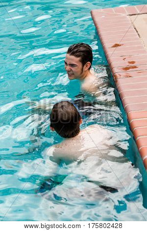 Brothers faving fun in outdoor swimming pool on hot summer day.