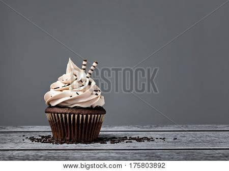 Chocolate cupcake with buttercream icing over a grey background
