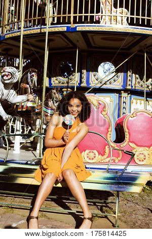 cool real modern teenage girl with candy near carousels at amusement park walking, having fun