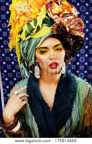 beauty bright woman with creative bright make up, many shawls on head like cubian, ethno look closeup