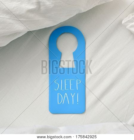 closeup of a blue door hanger with the text sleep day written in it, placed on a comfortable bed
