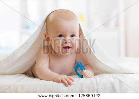 Smiling baby infant boy after shower or bath with teether toy covered towel in nursery. Health care concepts.