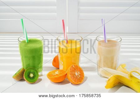Freshly blended fruit smoothies in glasses on a white wooden background. Fresh fruit cocktails of various colors and tastes kiwi banana orange. Assorted fruit shakes. Diet concept.