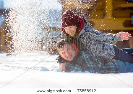 Young couple lies on the snow. The girl climbed onto the back of her boyfriend and sprinkled it with snow. Between them comic fight. Sunny winter day. Good mood. Young people smile