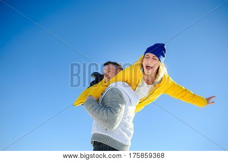 Young man holding in his arms his girlfriend. Man sturdily built easily picks up a fragile girl. Young people having fun. Against the background of the blue sky.