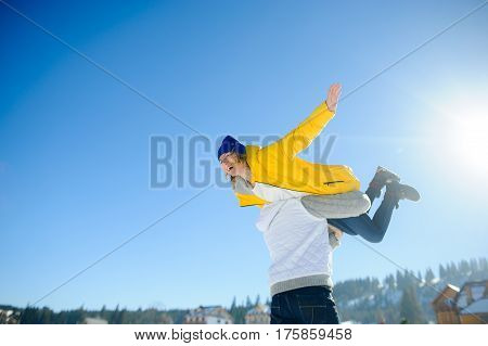 Young man holding in his arms his girlfriend. Man sturdily built easily picks up a fragile girl. Young people having fun. Against the background of the blue sky.