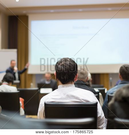Business and entrepreneurship symposium. Speaker giving a talk at business meeting. Audience in the conference hall. Rear view of unrecognized participant in audience.