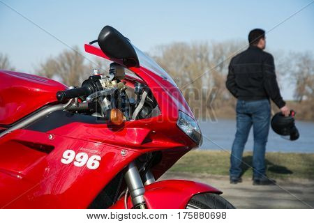 Senta, Serbia: March 4th, 2017. In focus beautiful red Ducati 996s motorcycle, photographed outdoor on a dock in Senta with driver and his helmet holding in his hand