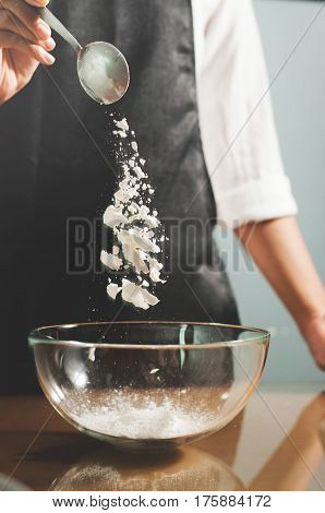 Woman chief sprinkling flour into glass bowl.