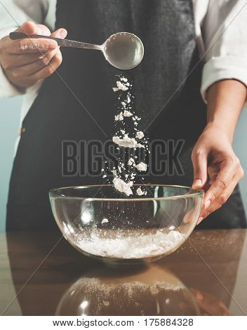Woman chief sprinkling flour into glass bowl.