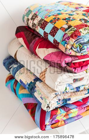 magnificent colored patchwork quilt put by a pile on a white court cupboard close up. a concept with scrappy blankets.