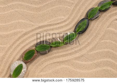Stones and green leaf on the sand with dunes and waves. Spa and zen concept. View from above