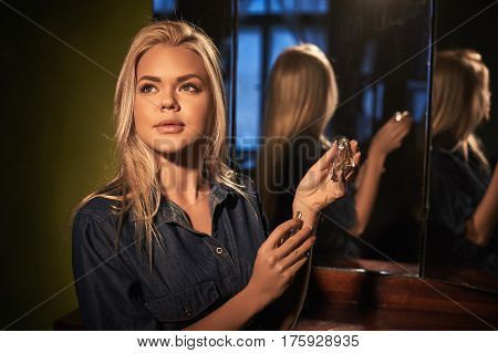 Young blonde beautiful woman wear perfume in retro bottle of perfume in console-mirror