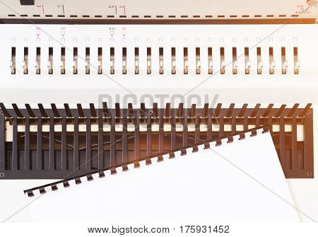 White paper on modern bookbinder tool closeup. White bookbinder in bright sunlight. Good office background.