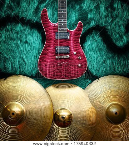 Purple electric guitar with three cymbals on turquoise color faux fur wall. Musical instruments background