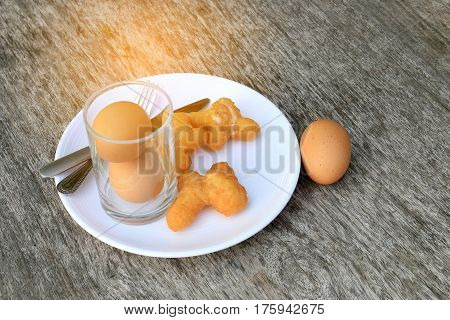 Fried Bread Stick Or Patongko And Soft-boiled Egg In White Dish With Fork And Knife On Wooden Backgr