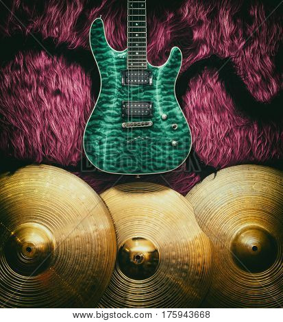 Green electric guitar with three cymbals on faux fur wall. Musical instruments background